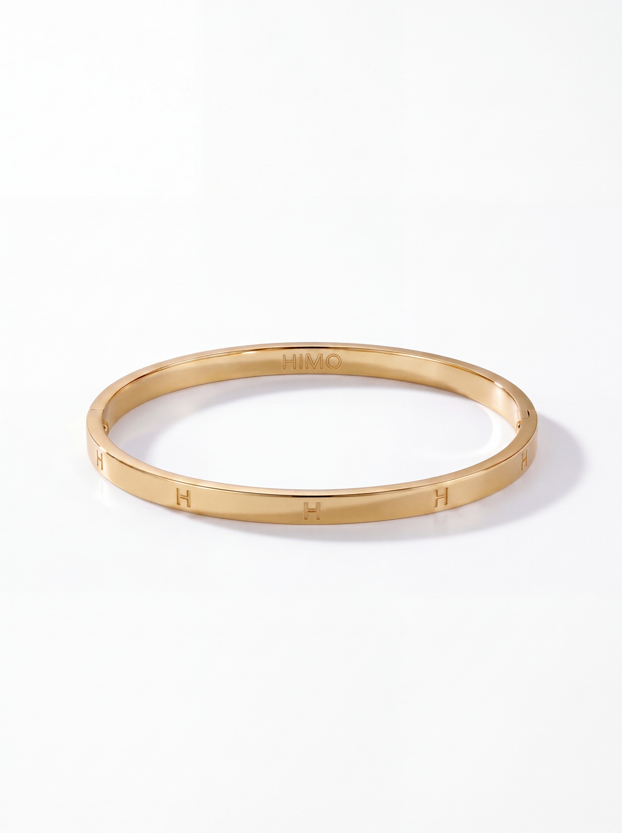 Classic H Bangle Small i 18K guldfärgad finish med H-gravyr från HIMO Signature på vit bakgrund.